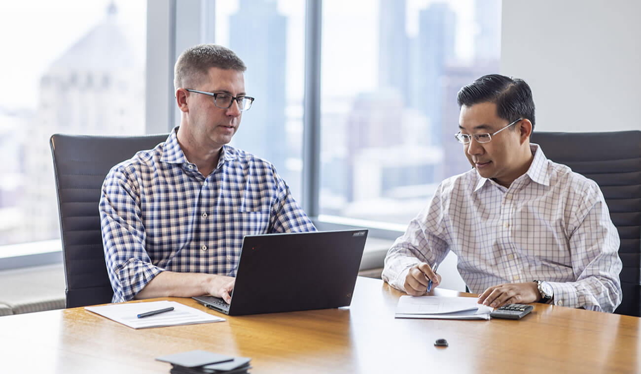Two men working at a table with a laptop.